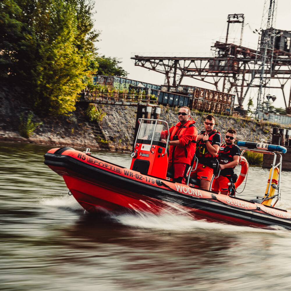 Ratownicy Wodni; Łódź motorowa płynąca po rzece, trzech załogantów.